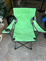 Light green folding chair fully open showing fabric seat and armrests with cup holders, black metal legs and frame visible.