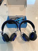 Two Jabra kids headphones in cobalt blue visible with cushioned ear pads and box containing underwater camera in background.