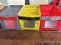 Set of three kids fabric storage bins on wooden surface, showing front mesh windows and handles