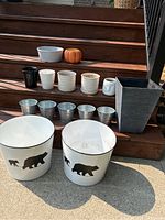 Wide view of assorted planters and pots on wooden stairs showing variety in sizes and designs, including large white bear-silhouetted planters and silver tin pots.