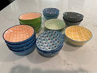 16 small porcelain bowls with distinct colorful geometric and floral patterns arranged on a marble countertop.