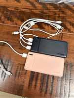 Both black and pink AsperX branded portable chargers with attached charging cables.
