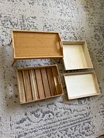 Four wooden trays, one with folding legs and three flat trays arranged on carpeted floor.
