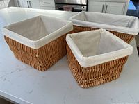 Three wicker storage baskets placed on a white countertop showing different sizes and fabric lining details.