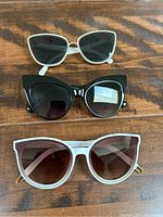 Three pairs of sunglasses on wooden surface showing different frame colors and styles.