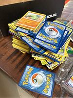 Photo showing a large pile of loose Pokémon trading cards with card fronts and backs visible on a wooden surface.