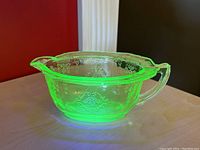 Side view of uranium green glass creamer dish under natural light showing etched Princess pattern and handle.