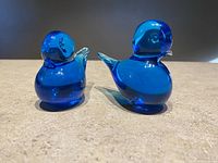 Two blue glass birds side by side showing rounded bodies, clear wings, and smooth cobalt blue glass