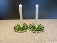 Pair of vintage green glass candle holders standing upright with white taper candles inserted, showing frontal view on table surface.