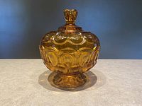 Front view of amber colored candy dish with lid closed, showcasing raised circular Moon and Stars pattern and flower-shaped finial.