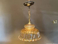 Full view of the iridescent carnival glass ceiling pendant light with brass mounting and chain against a beige wall.