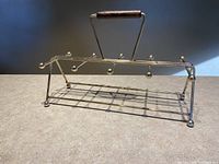 Full view of brass caddy showing eight protruding pegs for glasses and wooden handle.