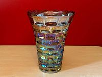 Full front view of the vintage Federal Glass carnival iridescent tulip vase on a wooden table against a red wall.