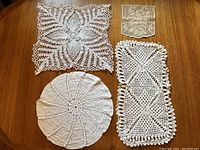 Four vintage crochet lace doilies arranged on wooden table: large round, small square, two rectangular