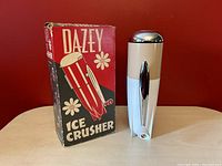 Dazey ice crusher with original box on left side, showing bullet shape and beige, white colors with chrome top.
