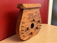 Wooden lyre-shaped door harp viewed from an angle showing tuning pegs and wood grain.
