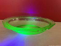 Side angle of the green uranium glass bowl showing the etched Florentine pattern glowing under UV light.