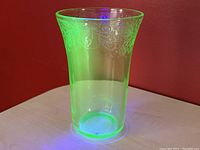 Green uranium glass tall tumbler under UV light, showing glowing effect and floral cameo pattern around upper edge.