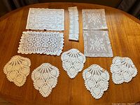 View of all nine vintage crochet doilies including five peacock feather shaped doilies and four rectangular floral doilies arranged on wooden surface.