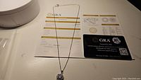 Full necklace with moissanite pendant, certification papers, and packaging shown on a white surface.