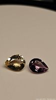Pair of pear cut natural gemstones on neutral background, featuring a purple amethyst and golden citrine side by side