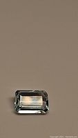 Clear photo of a rectangular emerald cut aquamarine gemstone with sky blue color on plain background.
