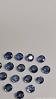 Photo showing multiple round cut denim blue sapphires arranged on a neutral background, highlighting their color and clarity.