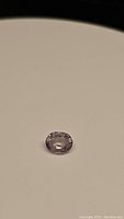 Single light purple oval cut sapphire gemstone placed on a beige surface, showing transparency, facets and shape clearly.