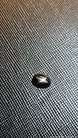 Photo of a single oval cabochon black star diopside gemstone showing a visible 4-ray star asterism effect under direct light.