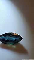 Close-up photo of marquis cut natural blue sapphire with green undertones, showing the gemstone's facets and color.