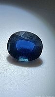 Close-up photo of oval cut natural blue sapphire gemstone showing facets and color under light.
