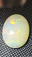 Close-up image of the natural untreated Ethiopian opal, oval cabochon showing rainbow flashes and smooth polished surface.