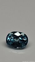 Photo of oval cut lagoon blue zircon gemstone under lighting showing facets and clarity