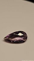 Pear-shaped purple amethyst gemstone with checkerboard cut on top, showing clarity and color from angled view.