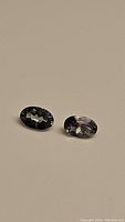 Pair of oval cut tanzanite gemstones showing blue-purple coloration and faceting details on neutral background.