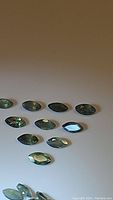 Photo showing multiple marquise cut alexandrite gemstones laid out on a flat surface, displaying a greenish color under normal lighting.