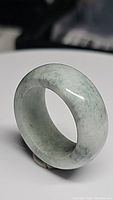 Close-up photo of a thick jade ring standing vertically on a flat white surface showing its smooth carved finish and natural stone pattern.