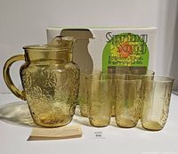 Photo of One amber glass pitcher with daisy pattern and six matching glasses in front of the original Spring Song box.