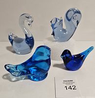 One photo showing four blue glass figurines including two birds, two swans, and one squirrel on a white surface with lot number card.