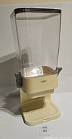 Front view of vintage cereal dispenser showing clear plastic container and beige base with lever