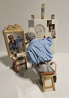 Front view of Norman Rockwell figurine seated on stool painting self-portrait at easel with mirror and table with art supplies