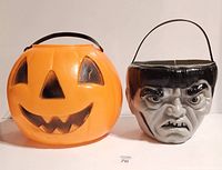 Both candy pails side by side on white surface, showing full frontal views of the pumpkin and Frankenstein's monster buckets.