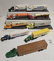 Photo of 7 diecast semi trucks with trailers arranged in two rows near white background.