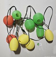 Photo showing full length of vintage patio string lights with multiple yellow, green, and orange ribbed blow molded lights on black cord.
