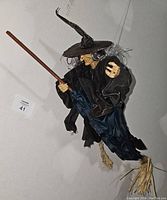 Vintage hanging witch decoration shown from side and angled views, details of face, clothing, broomstick and straw feet visible.