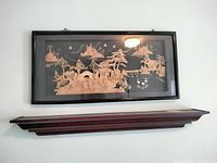 Frontal image of the antique carved cork diorama encased in a black wood frame hanging on a light-colored wall above a wooden shelf.