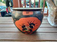 Front view of large round porcelain fishbowl planter pot with black and reddish-orange background and hand-painted koi fish and floral design.