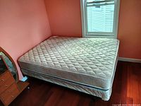 Full size mattress, box spring, and steel frame arranged in a bedroom corner with hardwood floors and salmon colored walls