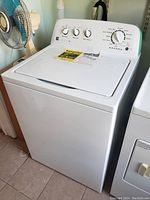 Front and side view of a white Kenmore top load washing machine with control panel and energy guide label on lid.