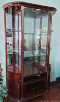 Front angled view of a solid wood redwood china cabinet showing curved glass panels and upper glass shelves for display.
